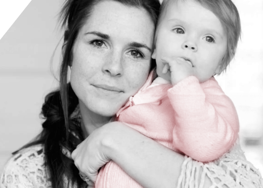 A black and white photo of a woman holding an infant who is wearing a pink onesie. [82]